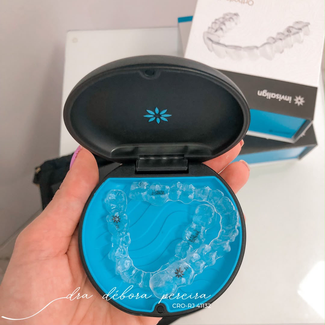 Alinhadores Invisalign transparentes em seu estojo, segurados pela Dra. Débora