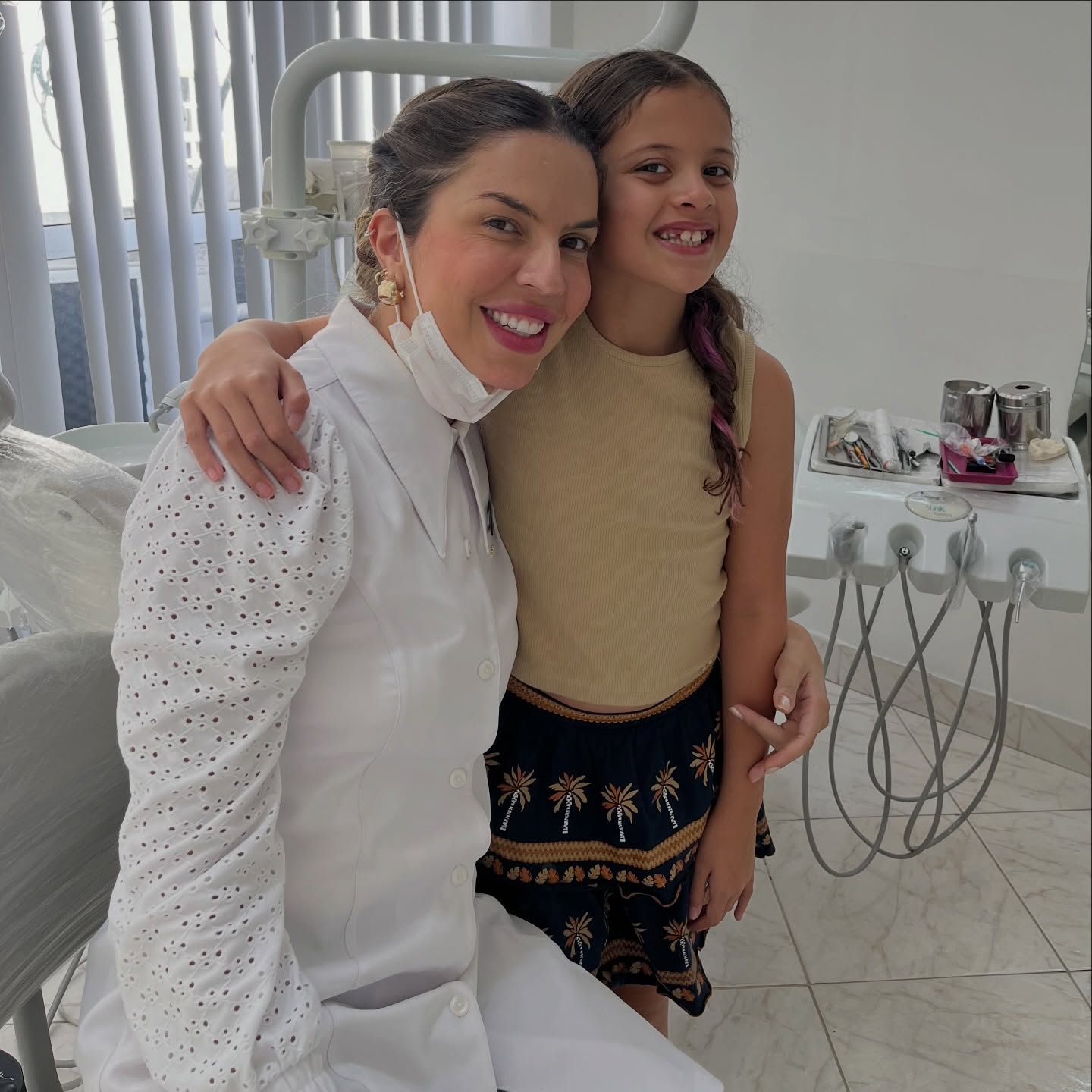 Dra. Débora Pereira sorrindo ao lado de uma paciente no consultório