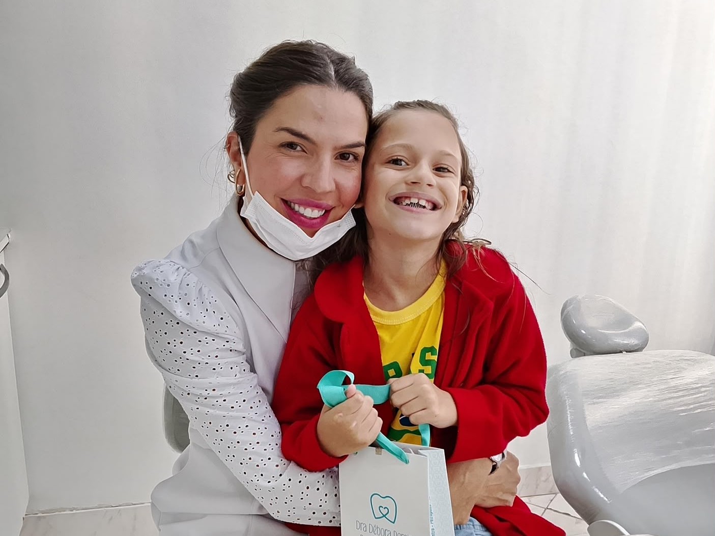 Dra. Débora abraçando criança sorridente após avaliação ortodôntica infantil